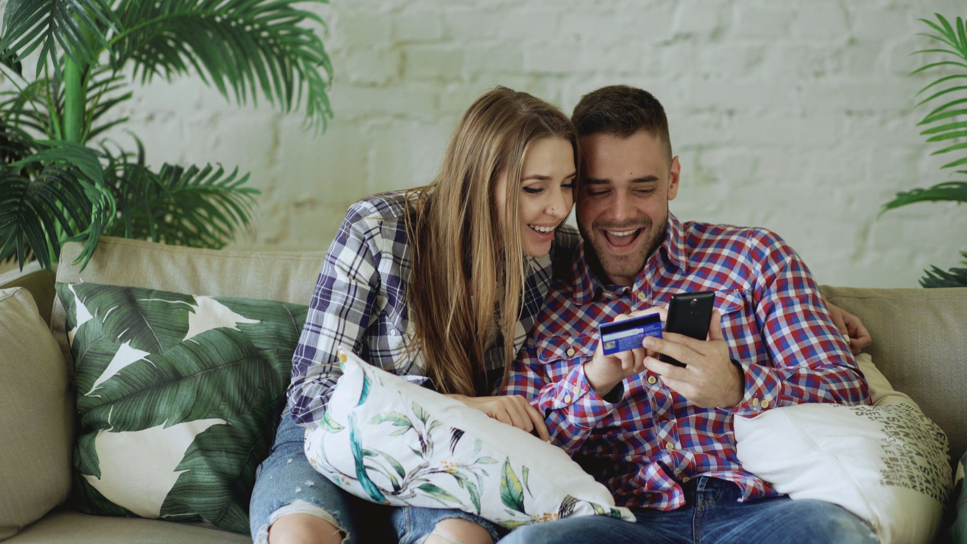 Uśmiechnięta para na kanapie przegląda zakupy online na smartfonie